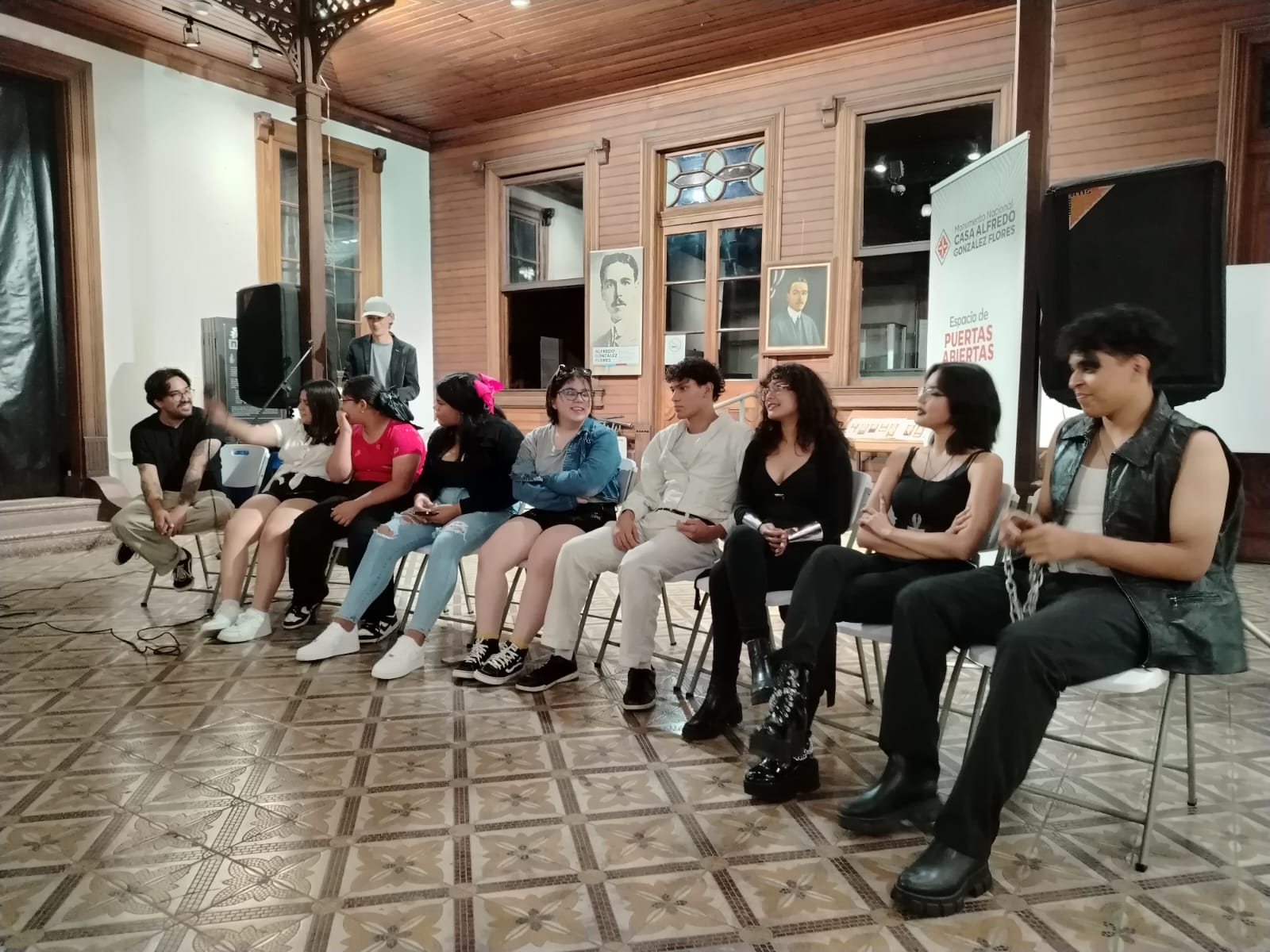 Grupo de jóvenes sentados en sillas alineadas hacia al frente, conversando o sonriendo