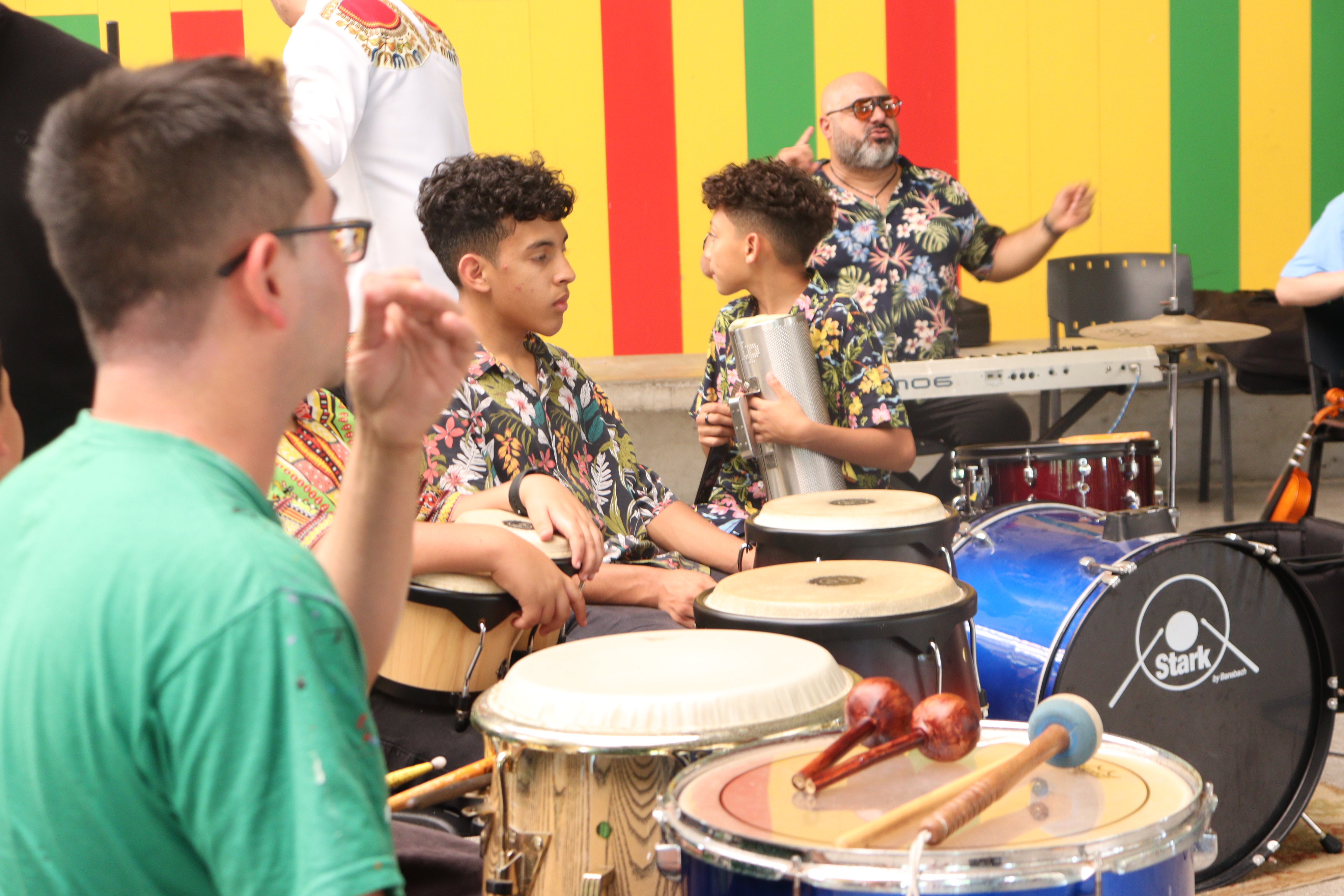 Jóvenes sentados frente a los timbales, al fondo un señor frente a un teclado.