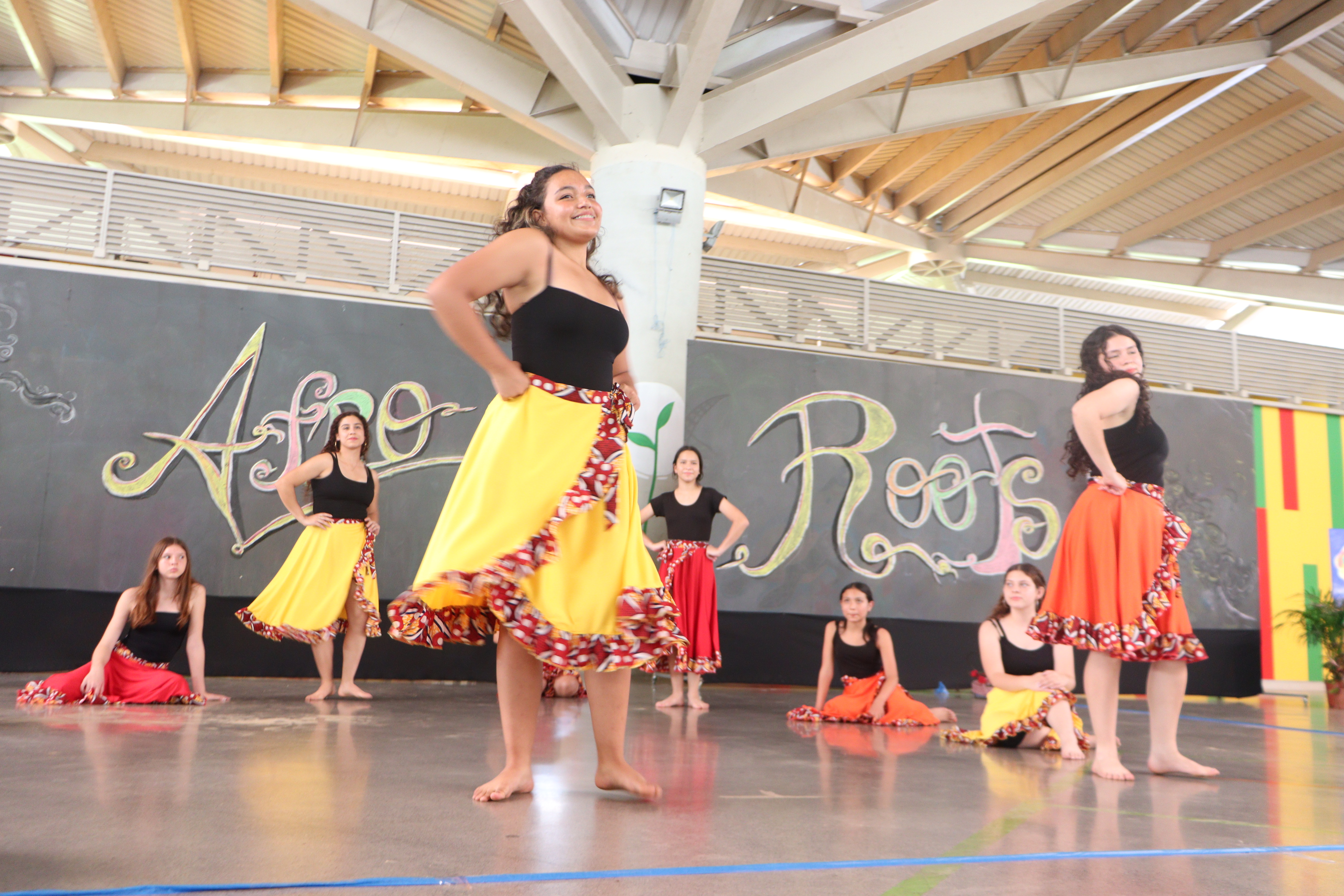 Mujeres jóvenes sonriendo mientras bailan, vestidas con enaguas. Al fondo se lee Afro Roots