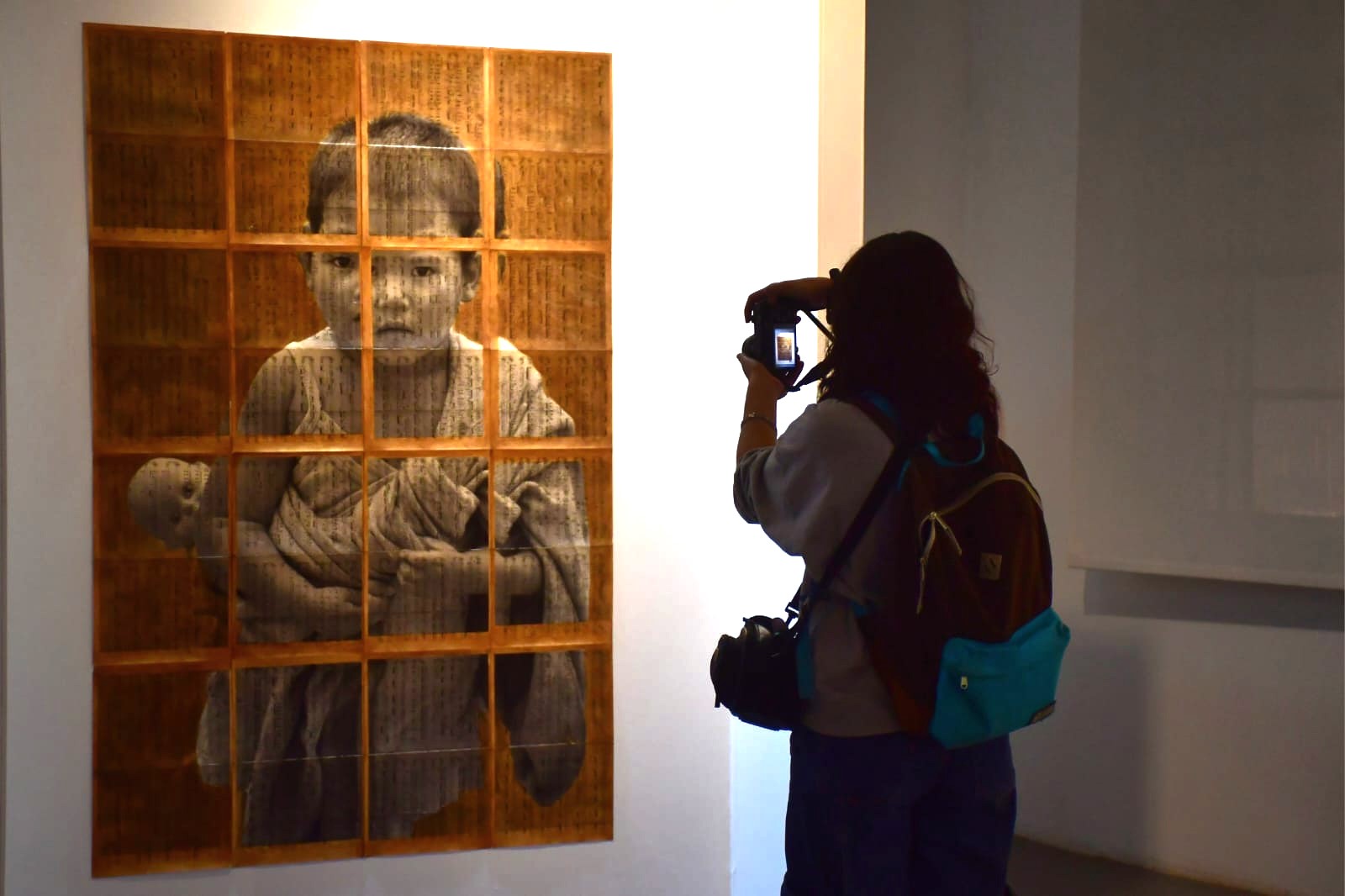 Una persona fotografiando una obra de un niño cargando un muñeco en su espalda