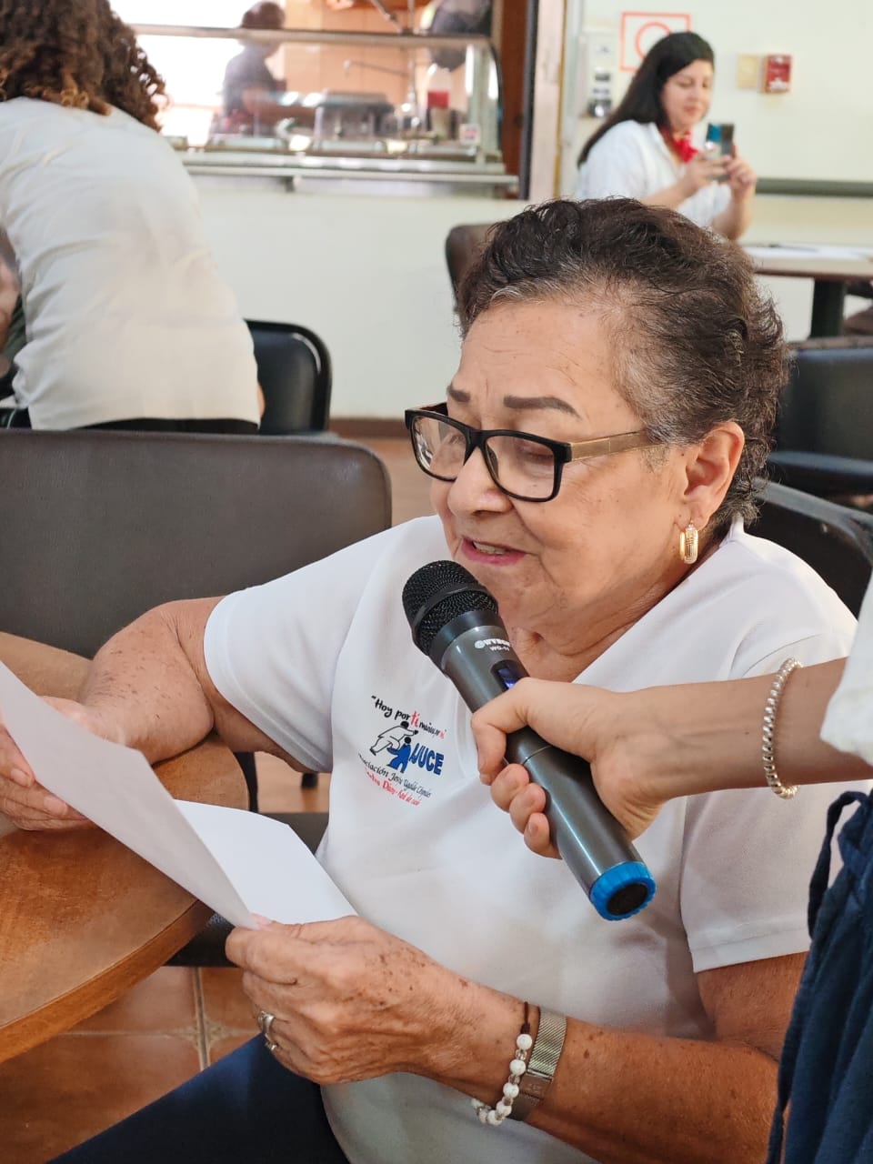Una señora sentada leyendo un papel y hablando a un micrófono