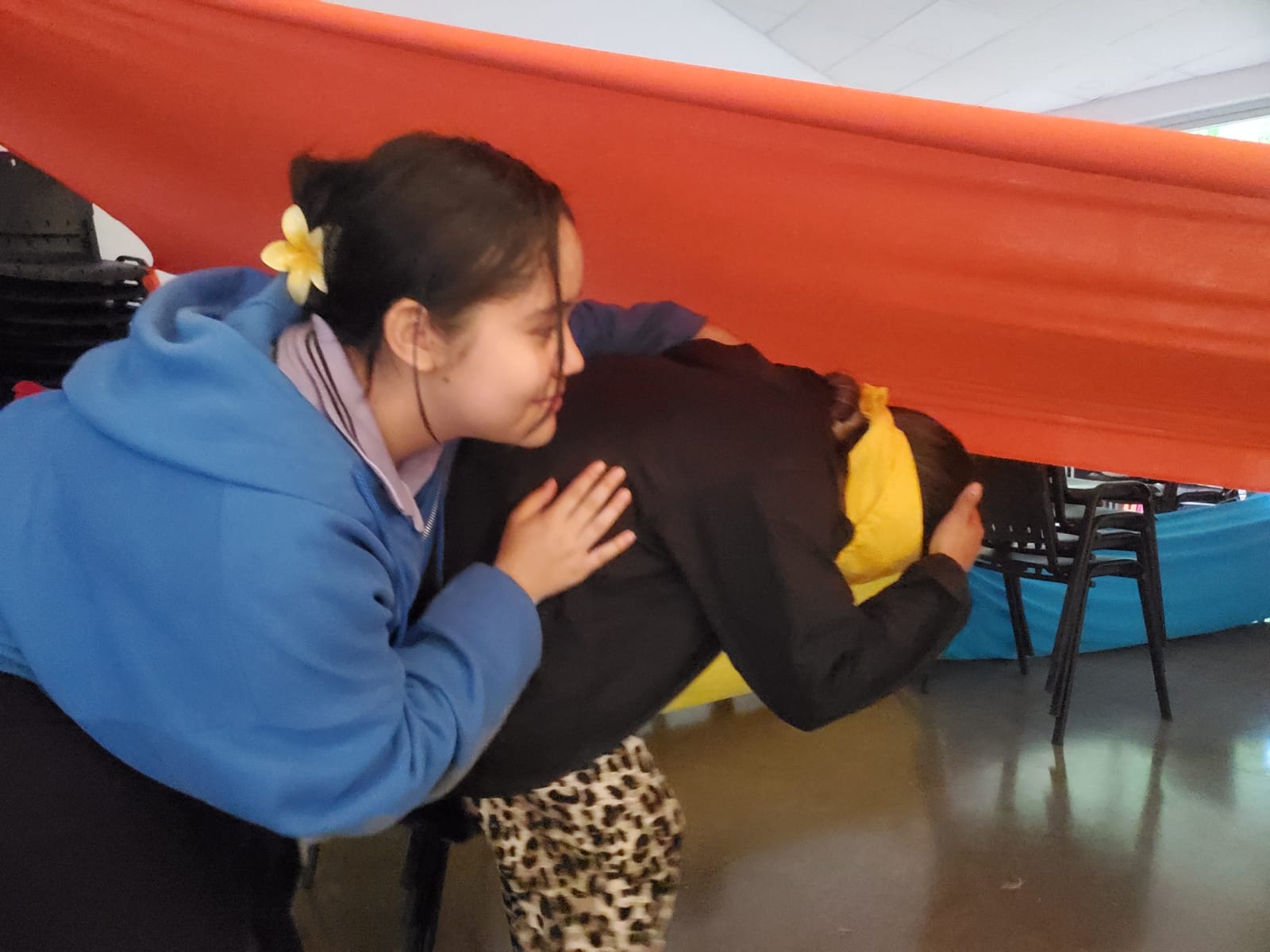 Dos niñas agachadas pasando debajo de una tela, una de ellas con los ojos vendados
