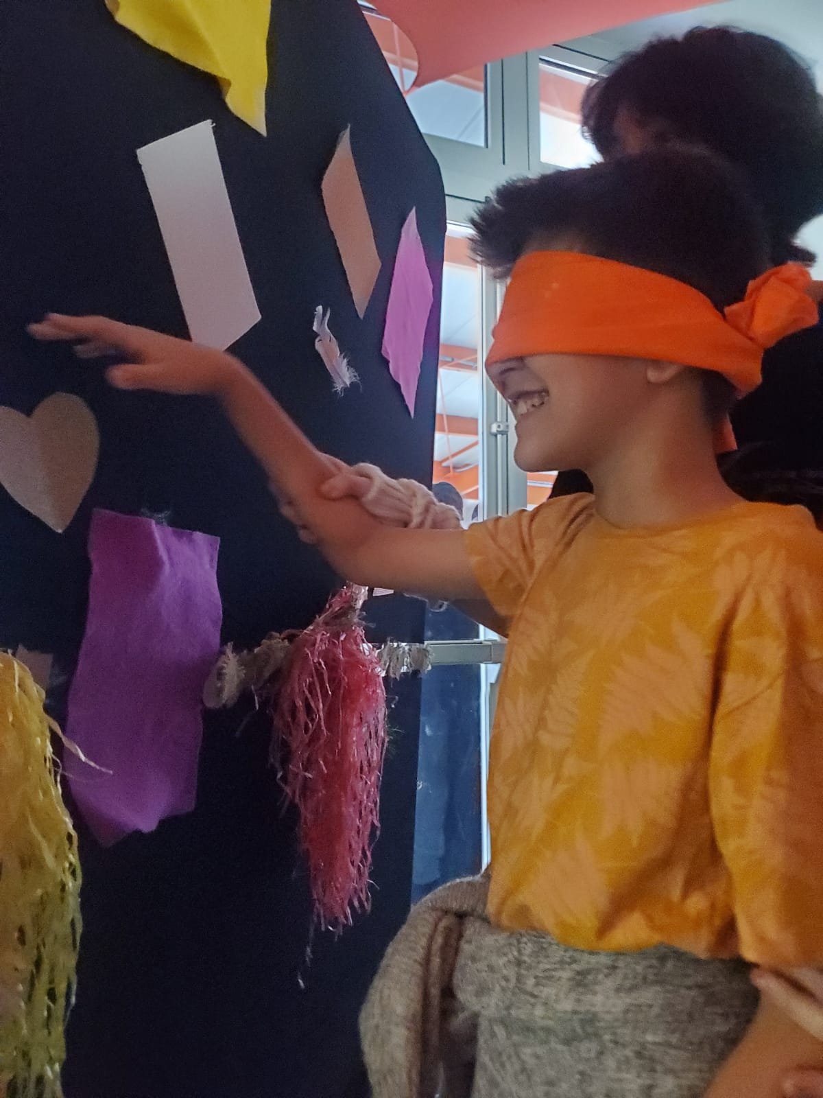 Una persona guía a un niño con los ojos vendados para tocar objetos en una pared