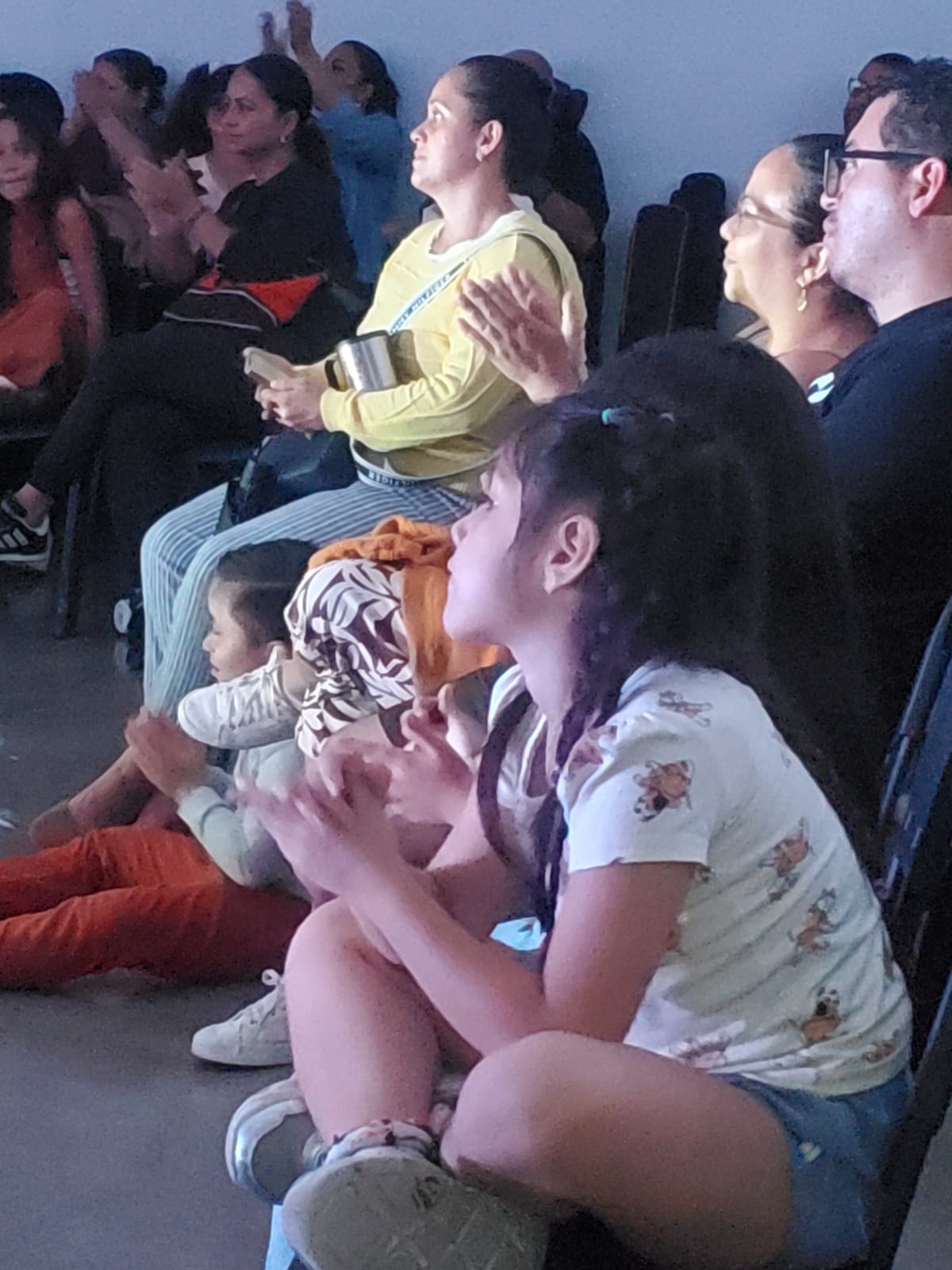 Personas sentadas en sillas y en el suelo aplaudiendo