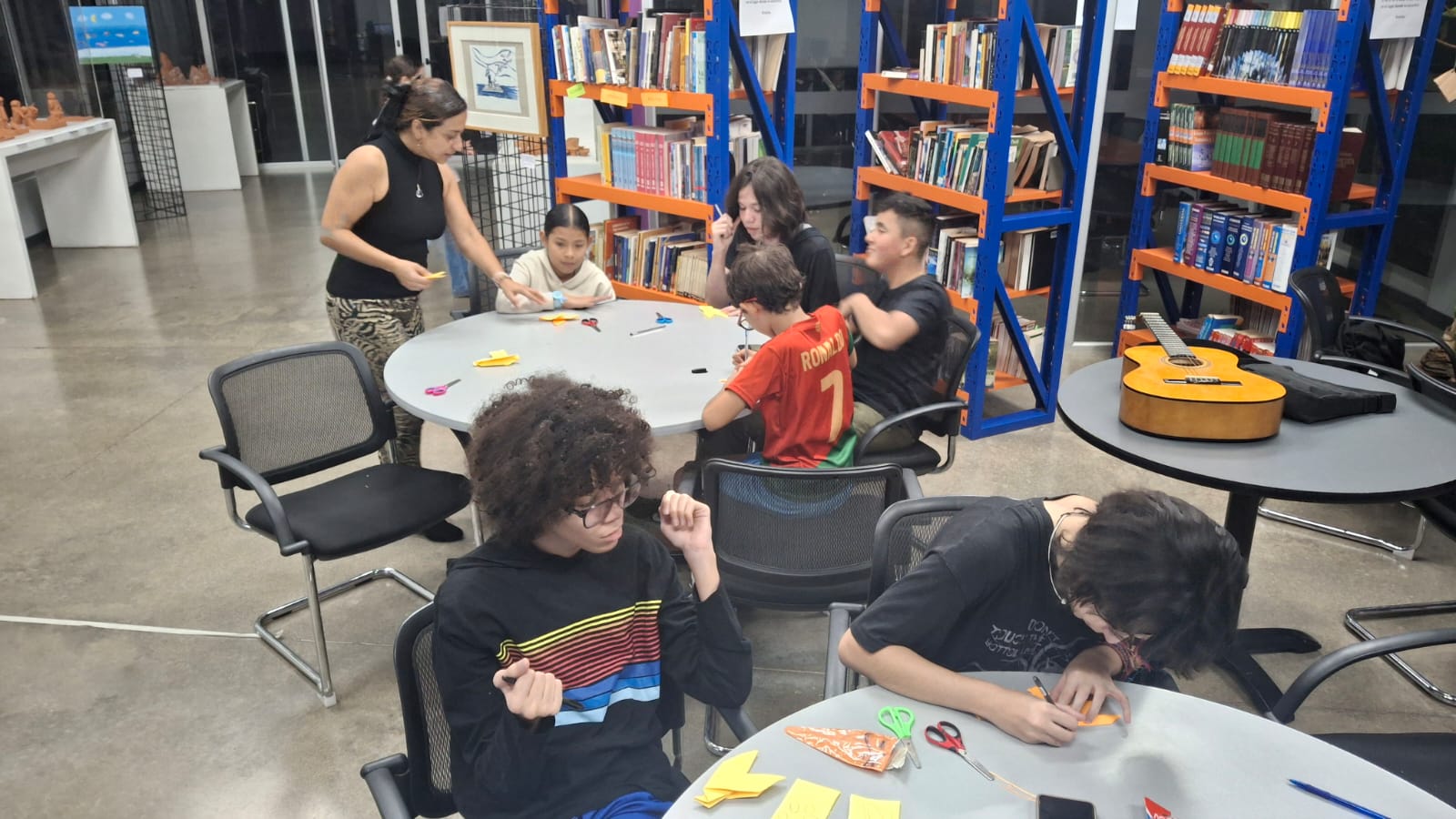 Jóvenes sentados en mesas redondas realizando paloma de papel y escribiendo