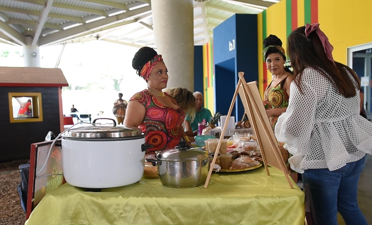 Mujer con vestimenta afrocaribeña frente a una mesa con comida
