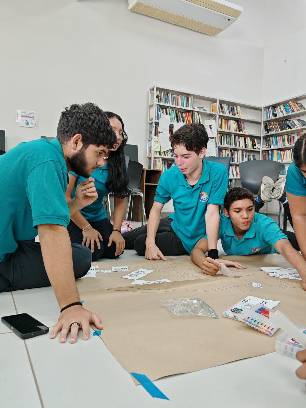 Jóvenes sentados en el piso trabajando sobre un papelografo