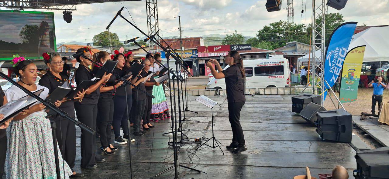 Mujer dirigiendo a un grupos de mujeres cantando, en una tarima