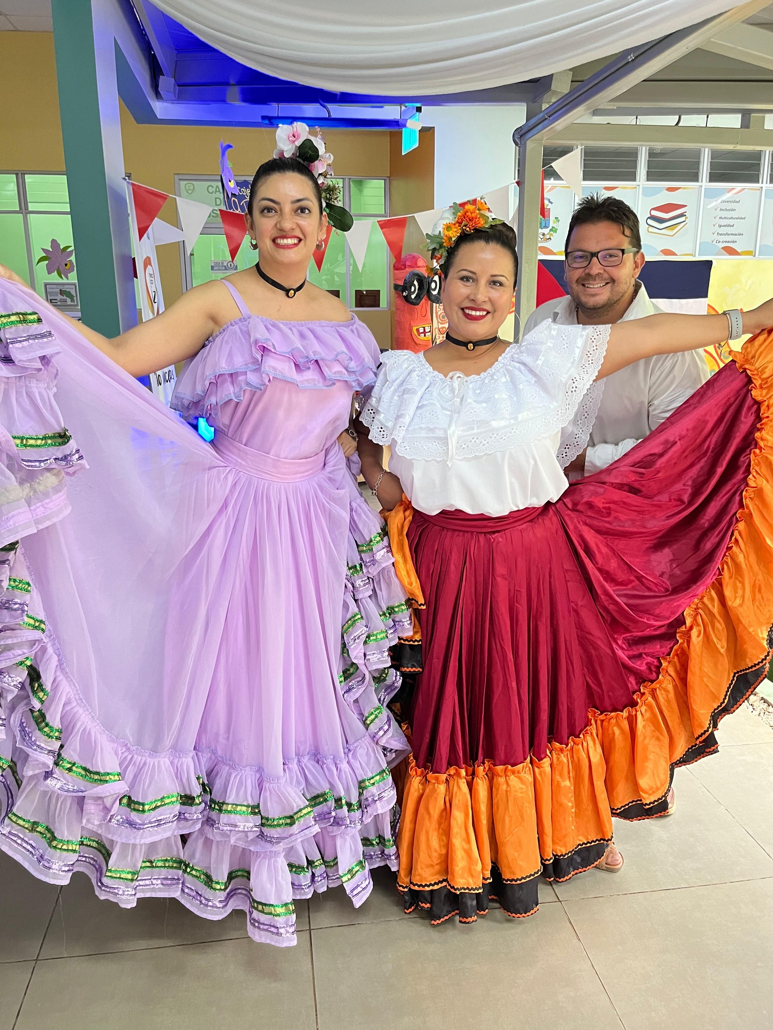 dos mujeres con traje tipico sonriendo y atrás un hombre con lentes sonriendo.