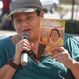 Imagen de una mujer hablando por micrófono y sosteniendo un libro con una caricatura de sí misma