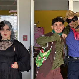 Mujer joven vestida de negro, y dos jóvenes vestidos mirando al frente