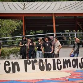 Jovenes atrás de una pared con grafitti que dice &amp;quot;en problemas&amp;quot;