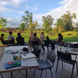 Jovenes pintando en mesas blancas y de fondo arboles