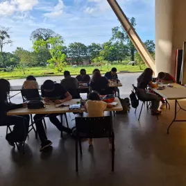 Jovenes pintando en mesas blancas y de fondo arboles